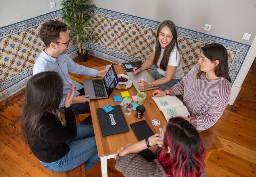 Group of five people working together around a table with laptops, notebooks, and post-it notes