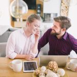 A man and woman seated at a table, collaborating on a laptop together