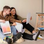 A couple sitting on the floor, reviewing documents and papers together with focused expressions