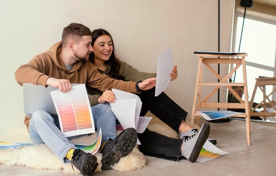 A couple sitting on the floor, reviewing documents and papers together with focused expressions